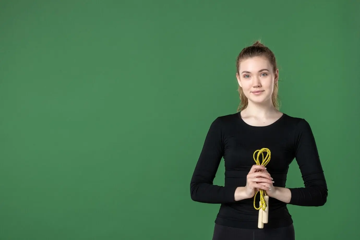 Frontansicht einer jungen Frau, die ein Springseil hält, vor grünem Hintergrund; Gesundheit, Frau, Workout, Farbe, Sport, Gymnastik, Körper.