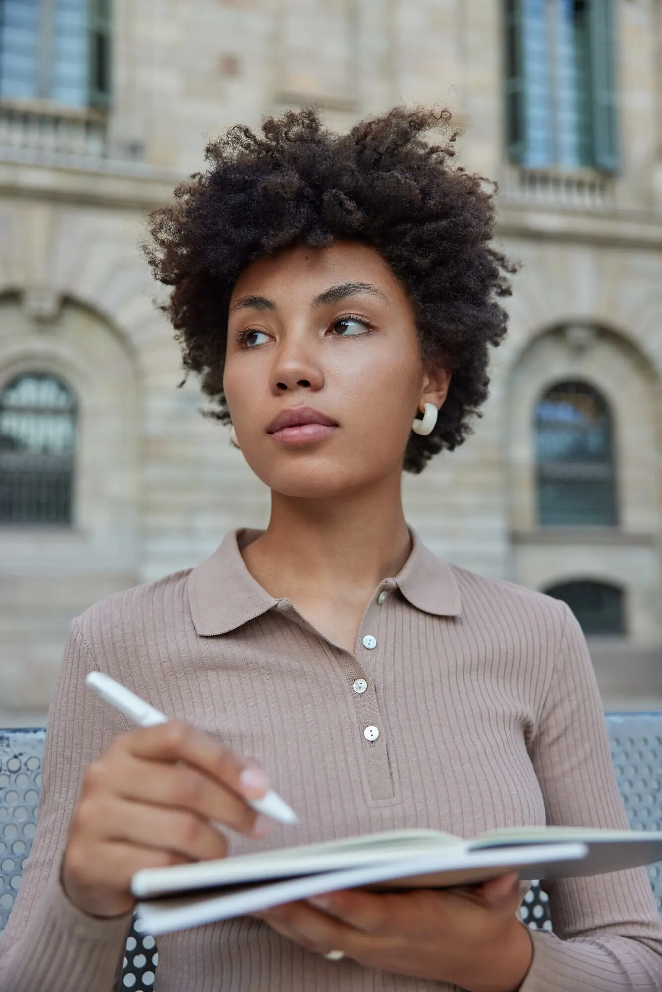 Eine Frau verbringt ihre Freizeit gern mit ihrem Hobby, macht Notizen zum Lernen, hält Notizblock und Stift und schreibt Ideen für eine Veröffentlichung in ihr Notizbuch; sie trägt einen lässigen Pullover und posiert im Freien.